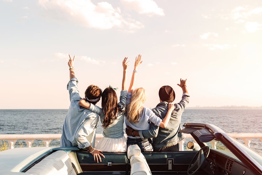 Vista posterior de jóvenes amigos felices parados con las manos levantadas cerca del coche